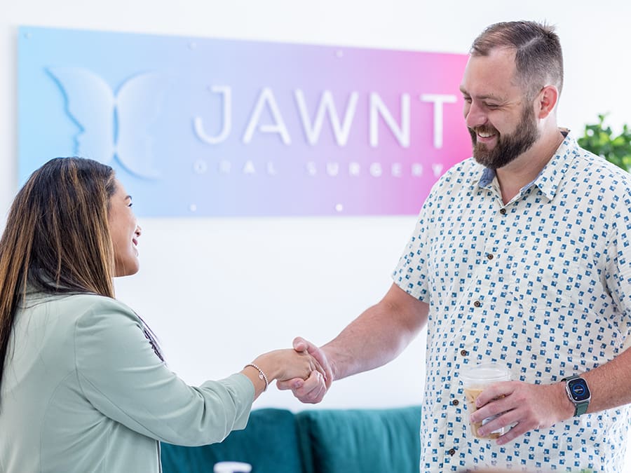 A patient shaking hands with the receptionist at JAWNT Oral Surgery